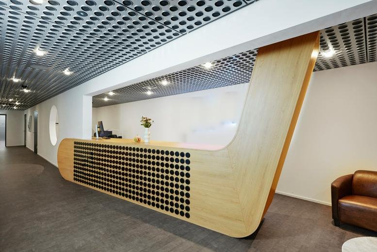 Modern wooden reception desk at Vulkanstrasse 130b with a unique curved design and perforated detailing.