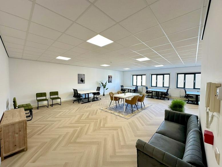 Spacious communal lounge with a grey sofa and wooden herringbone flooring.