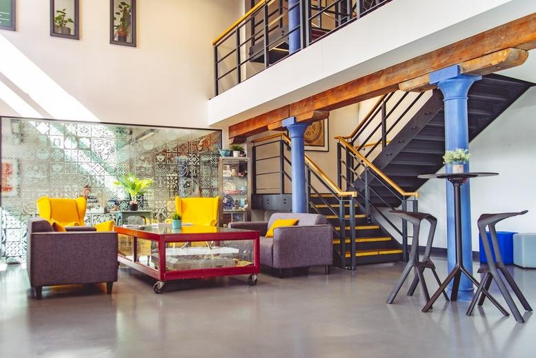 Spacious communal lounge at Walker Road, Newcastle, with yellow armchairs, a mezzanine level, and blue industrial pillars.