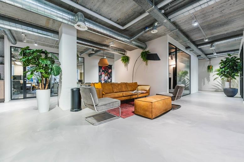 Spacious communal lounge at Westblaak 90 with velvet sofas, exposed ducting, and lush indoor plants.