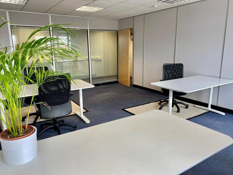 Spacious three-desk private office at Weston Centre Business Hub with a large potted plant and glass partition walls.