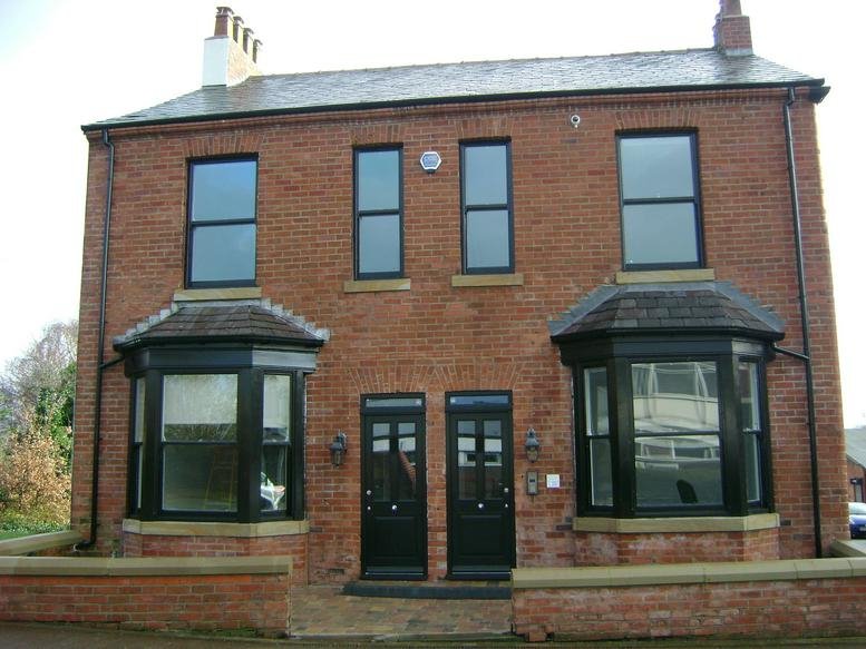 Red brick exterior of Westway House, Bridge Street, Newton Le Willows with black-framed windows and twin front doors.