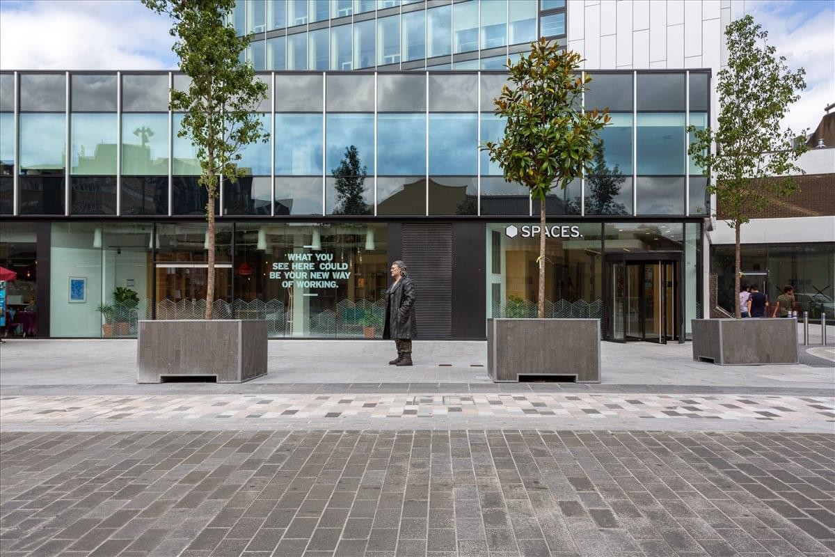 Exterior view of the glass-facade Woking One building with young trees out front.