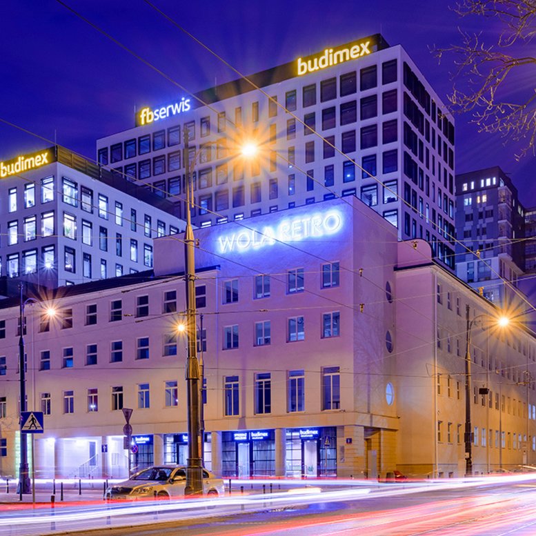 Dusk view of the modern Wola Retro office complex with bright signage and street lights.