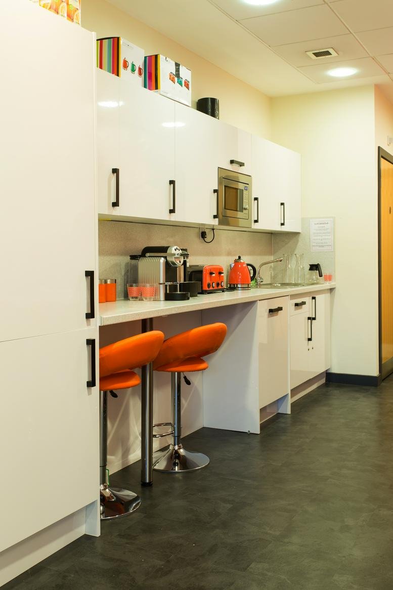 Modern white kitchen and breakout area with orange bar stools and integrated appliances.