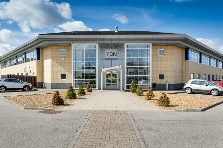 The exterior of the YBN building at 7-8 Delta Bank Road, featuring a modern glass facade and paved entrance.