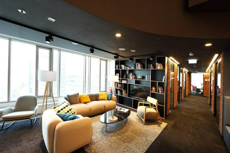 Spacious communal lounge with a large beige sofa, colorful pillows, and a modern bookshelf wall.