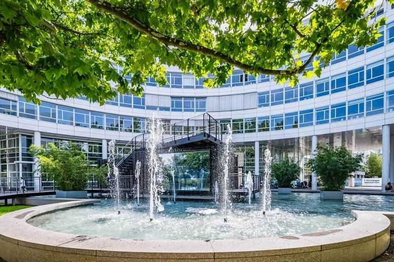 Exterior view of the curved glass-facade building at St. -Martin-Straße with a central courtyard fountain.