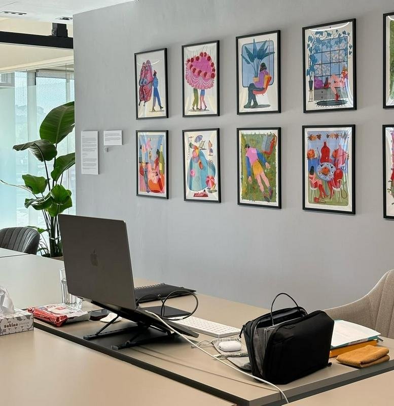 Open-plan office with art on the walls and a laptop on a desk.