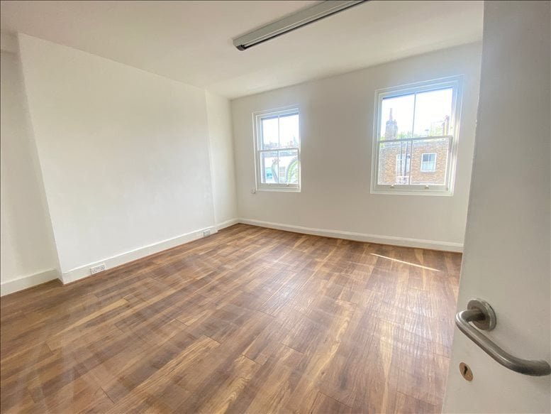 Empty room with wooden flooring and two large windows.