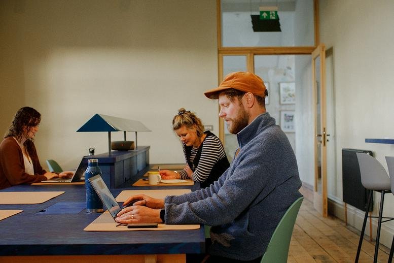 People working at long blue tables in a coworking space at The Ladder, 2 - 4, Clinton Road.