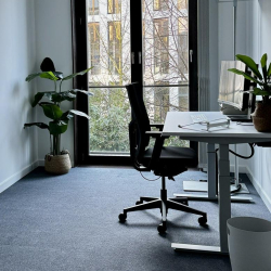 Modern private office with a height-adjustable desk, ergonomic chair, and large garden-facing window.