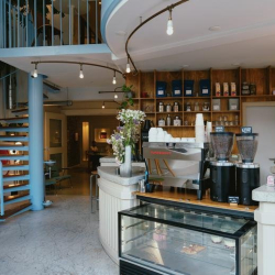 Cafe and reception area with coffee grinders, a pastry display, and bar seating.