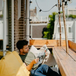 Sunny rooftop terrace with a man reading a newspaper on comfortable seating.
