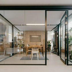 Transparent glass meeting pod with a wooden table and white designer chairs.