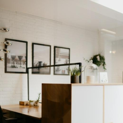 Minimalist workspace with white brick walls, framed artwork, and a black mesh chair.