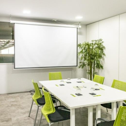 Meeting room featuring a white table, lime green chairs, and a large wall-mounted projector screen.