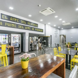 Industrial-style breakroom with wooden tables, yellow metal stools, and motivational wall text.