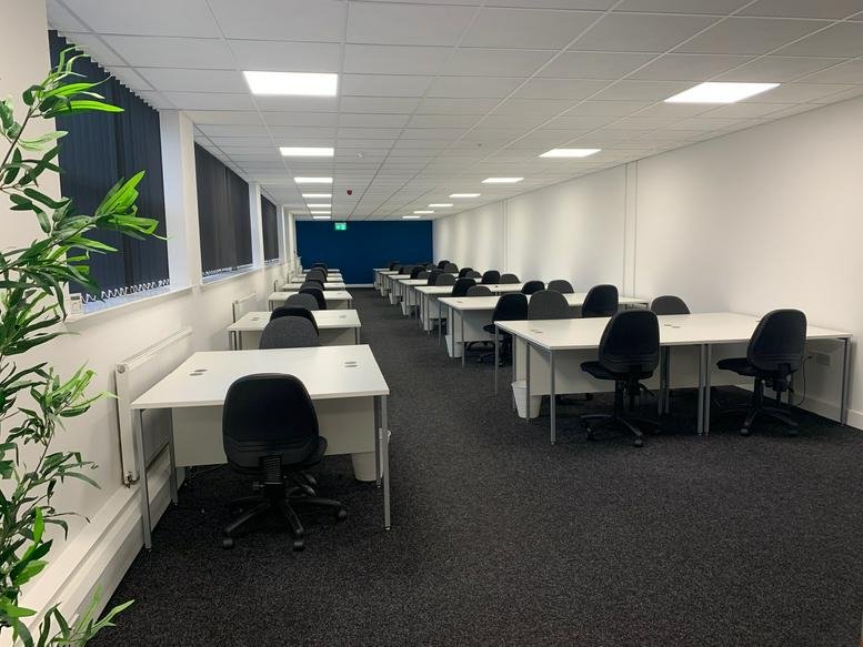 Spacious open-plan workspace with multiple desk pods and black office chairs.