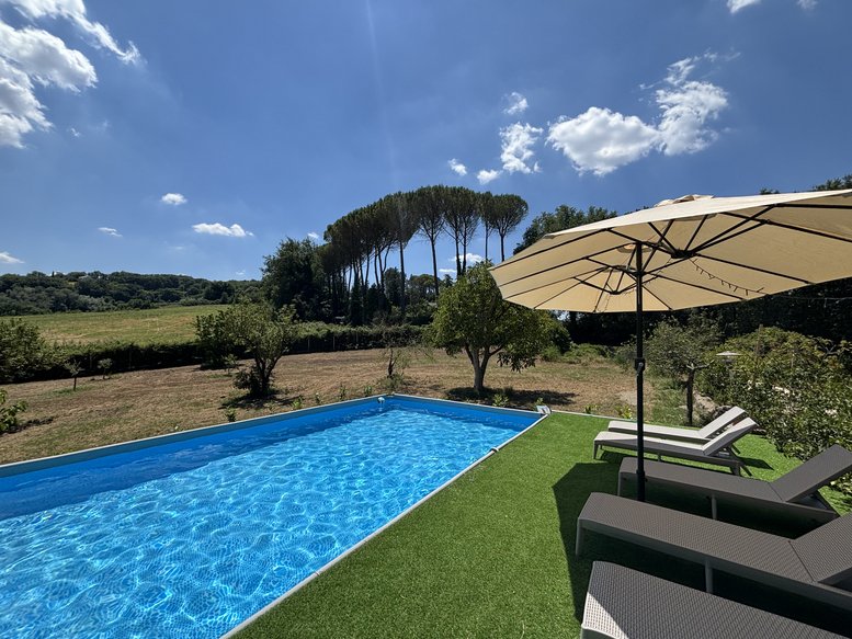 Blue outdoor swimming pool at Vocabolo Villa Alberti surrounded by green lawn and sun loungers.