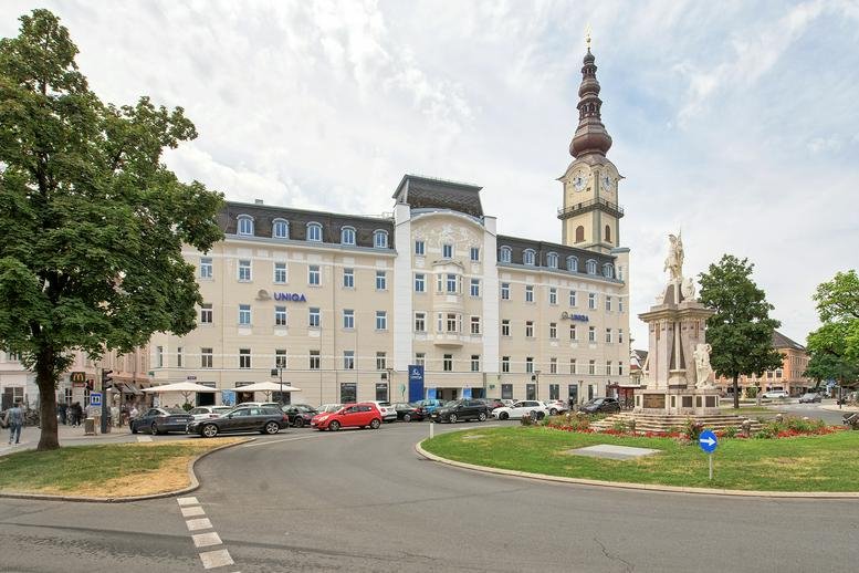 Grand historic building facade with a prominent clock tower and open square.